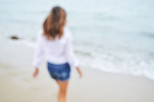 Woman wearing a white top and denim shorts walking towards the ocean on a beach